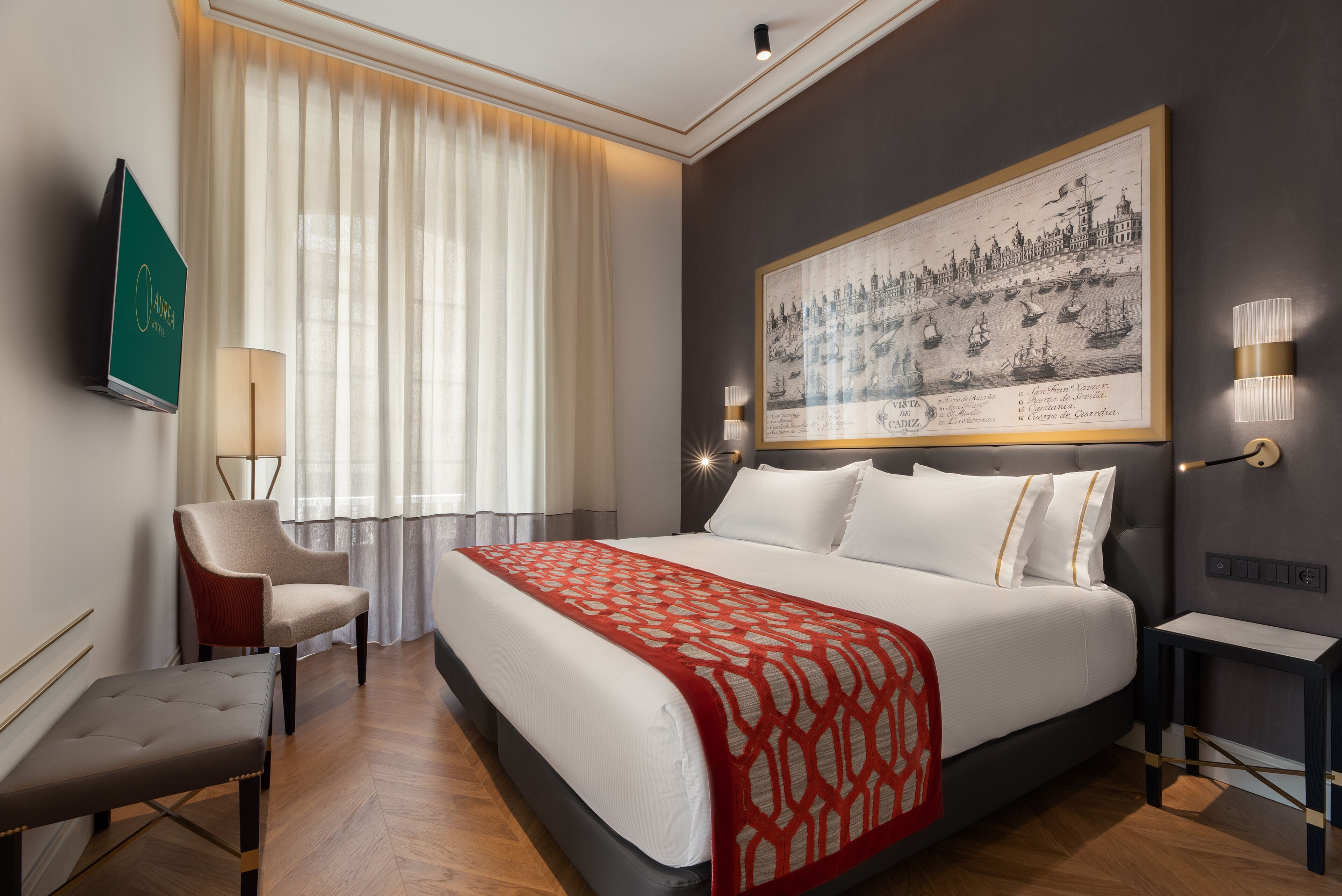 A hotel room with a large bed, a chair, a desk, and a wall-mounted TV.