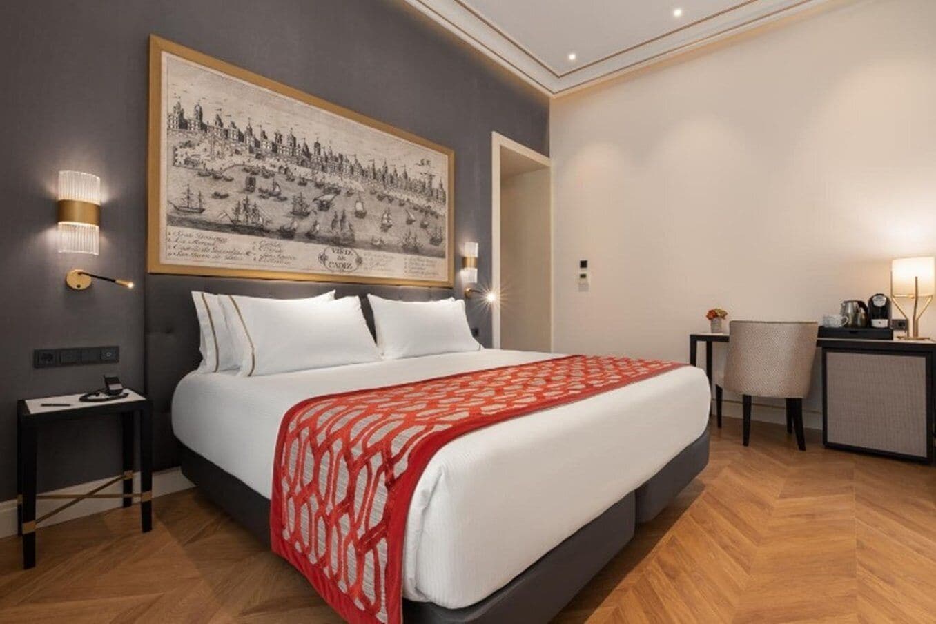 Ein Hotelzimmer mit einem großen Bett, einem Schreibtisch, einem Sessel und einem Wandbild.