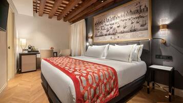 Una habitación de hotel moderna con una cama grande, vigas de madera en el techo, un mapa grande enmarcado en la pared y un pequeño escritorio con una lámpara.