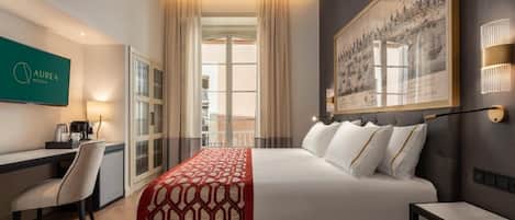 Habitación de hotel con cama, escritorio, silla, televisión y un ventanal grande.