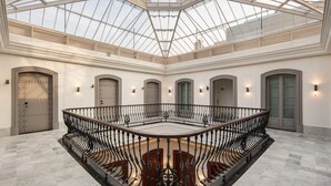 A spacious atrium with a glass ceiling, multiple doors, and a central staircase with ornate railings. - Áurea Casa Palacio Sagasta By Eurostars Hotel Company (Cádiz)