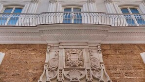 A building facade with ornate architectural details, including a balcony with white balustrades and a central decorative element featuring a coat of arms. - Áurea Casa Palacio Sagasta By Eurostars Hotel Company (Cádiz)