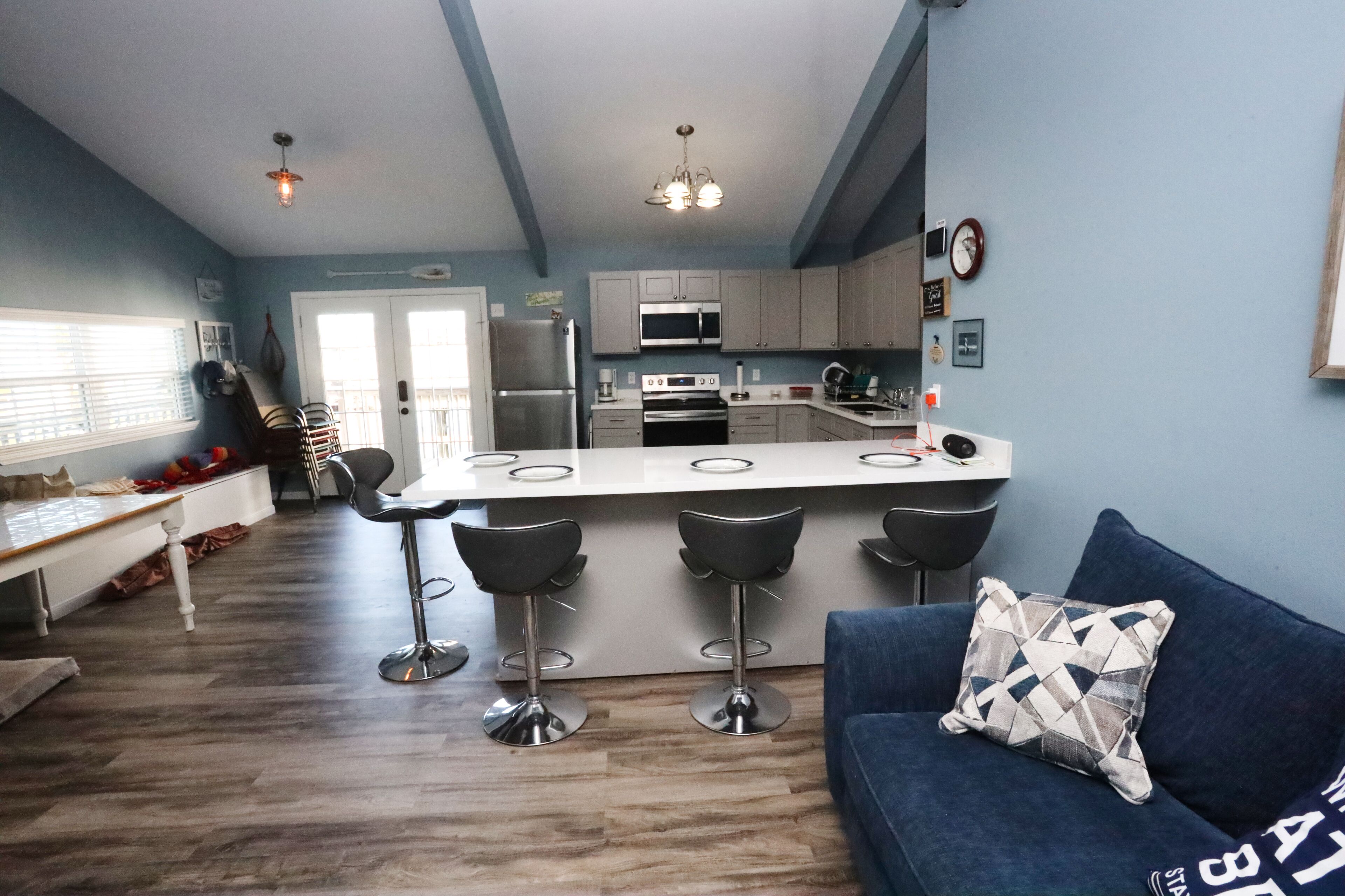 A modern kitchen with a central island, bar stools, and a blue sofa with a patterned pillow.