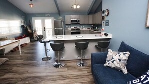 A modern kitchen with a central island, bar stools, and a blue sofa with a patterned pillow.