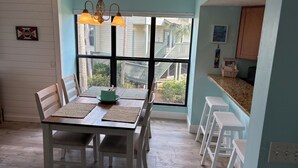 A dining area with a table set for four, a window with a view of a balcony, and a kitchen area with white bar stools. - Waterfront condo located in the waterfront paradise of Bokeelia (Bokeelia)