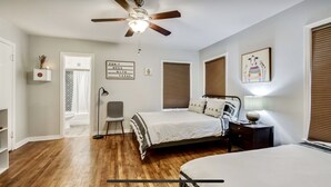 Ein Schlafzimmer mit einem Bett, einem Schreibtisch, einem Stuhl, einem Deckenventilator und einem an der Wand befestigten Regal.