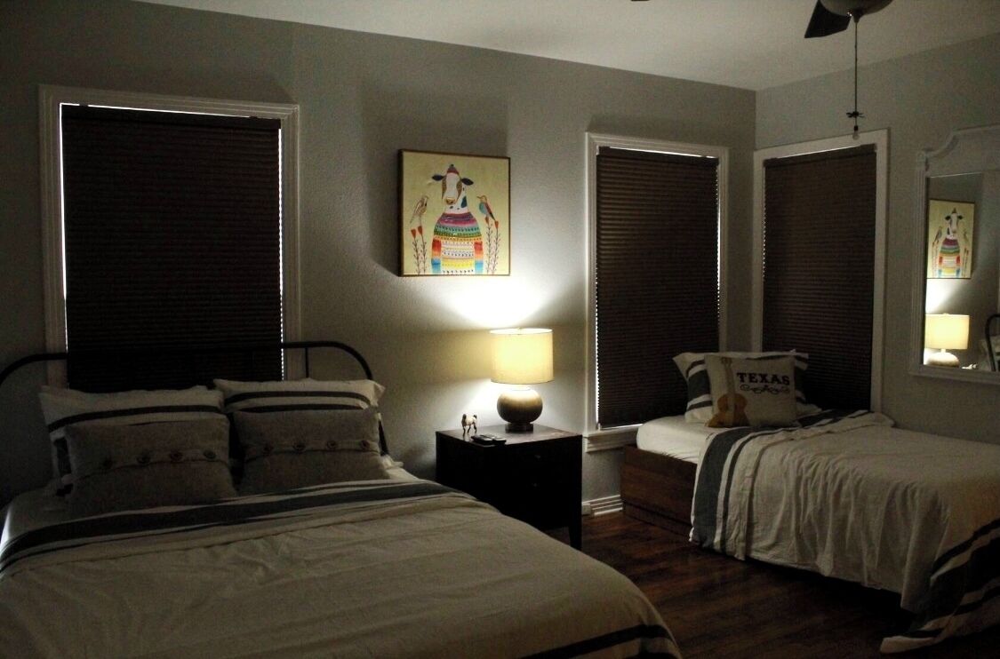 Een slaapkamer met een groot bed, een kleiner bed, een nachtkastje met een lamp en een wanddecoratie.
