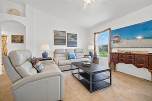 Relax in this stylish living room with a sofa, coffee table, and wooden cabinet, offering a view of the beach and lifeguard tower.