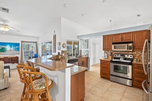 Een ruime keuken met een centraal eiland, houten kastjes, roestvrijstalen apparatuur en een eetgedeelte met rieten stoelen.