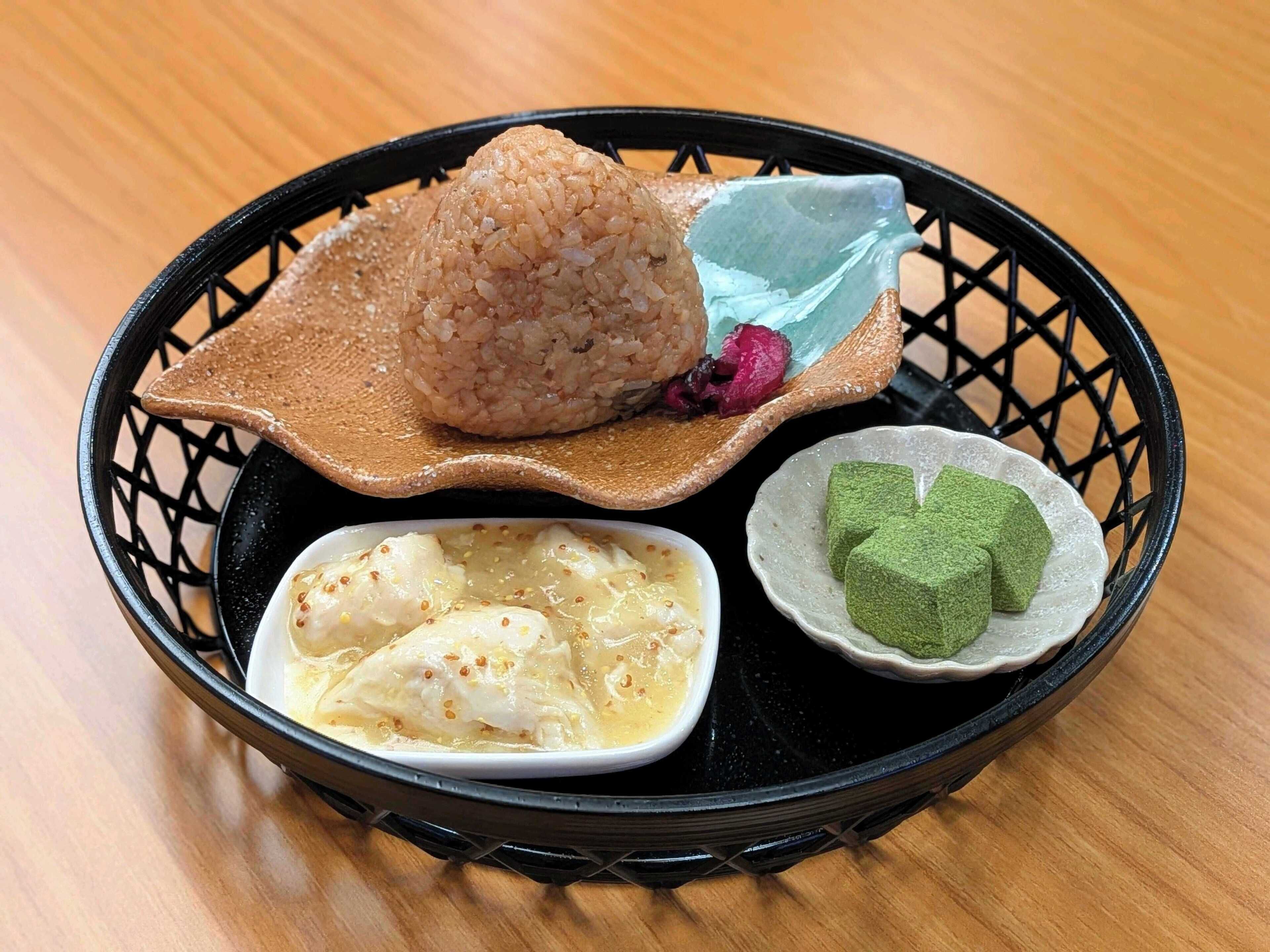 A meal with rice, fish, and green sweets on a black tray.