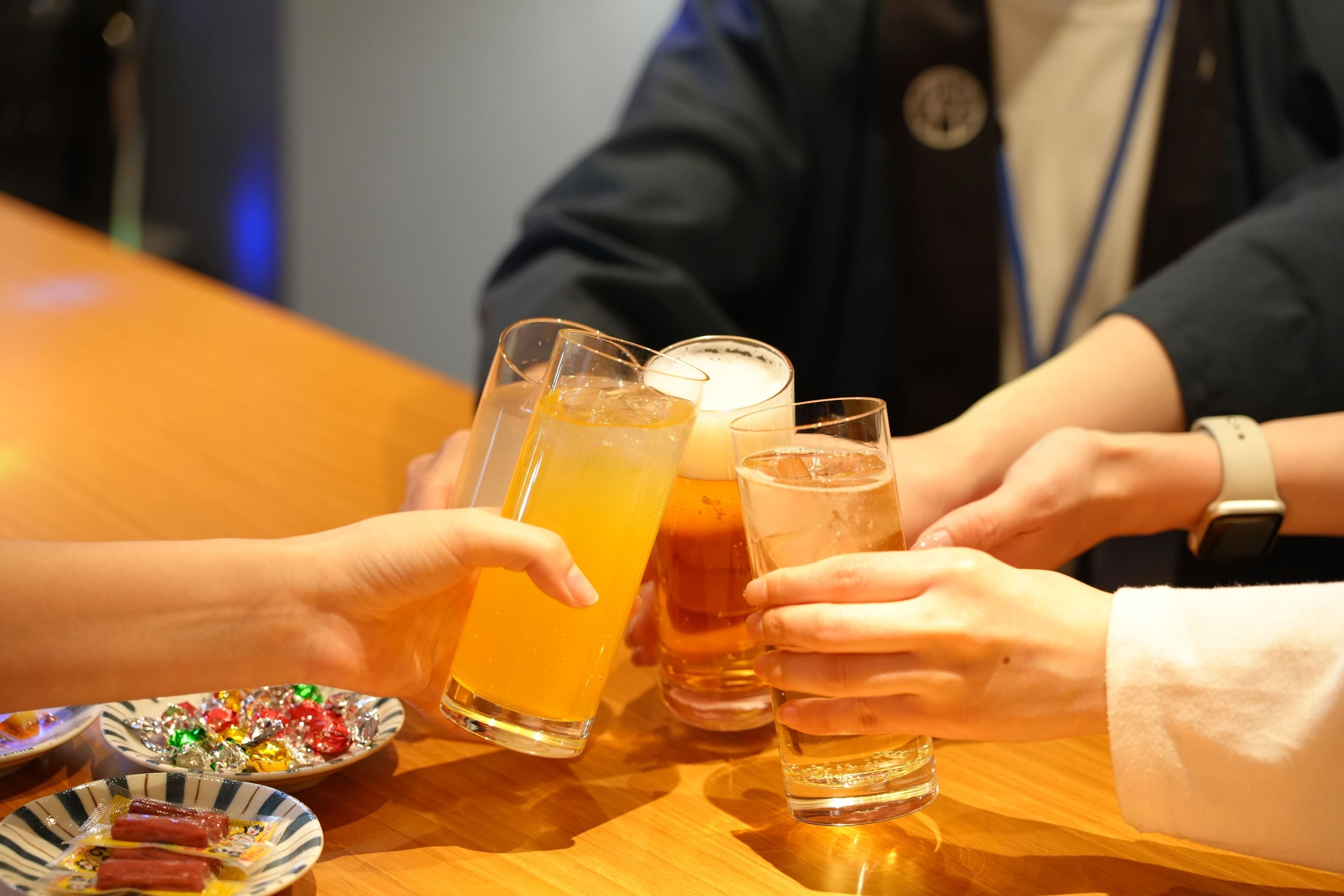 Un grup de persones brindant amb gots de cervesa a una taula de fusta amb plats d'aperitius.