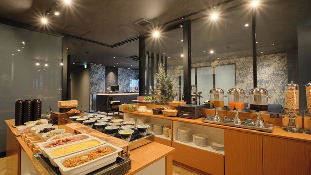 A buffet with various food items and beverages, a counter with a cash register, and a seating area with a view of the cityscape. - HOTEL SUI HAMAMATSU (Hamamatsu)