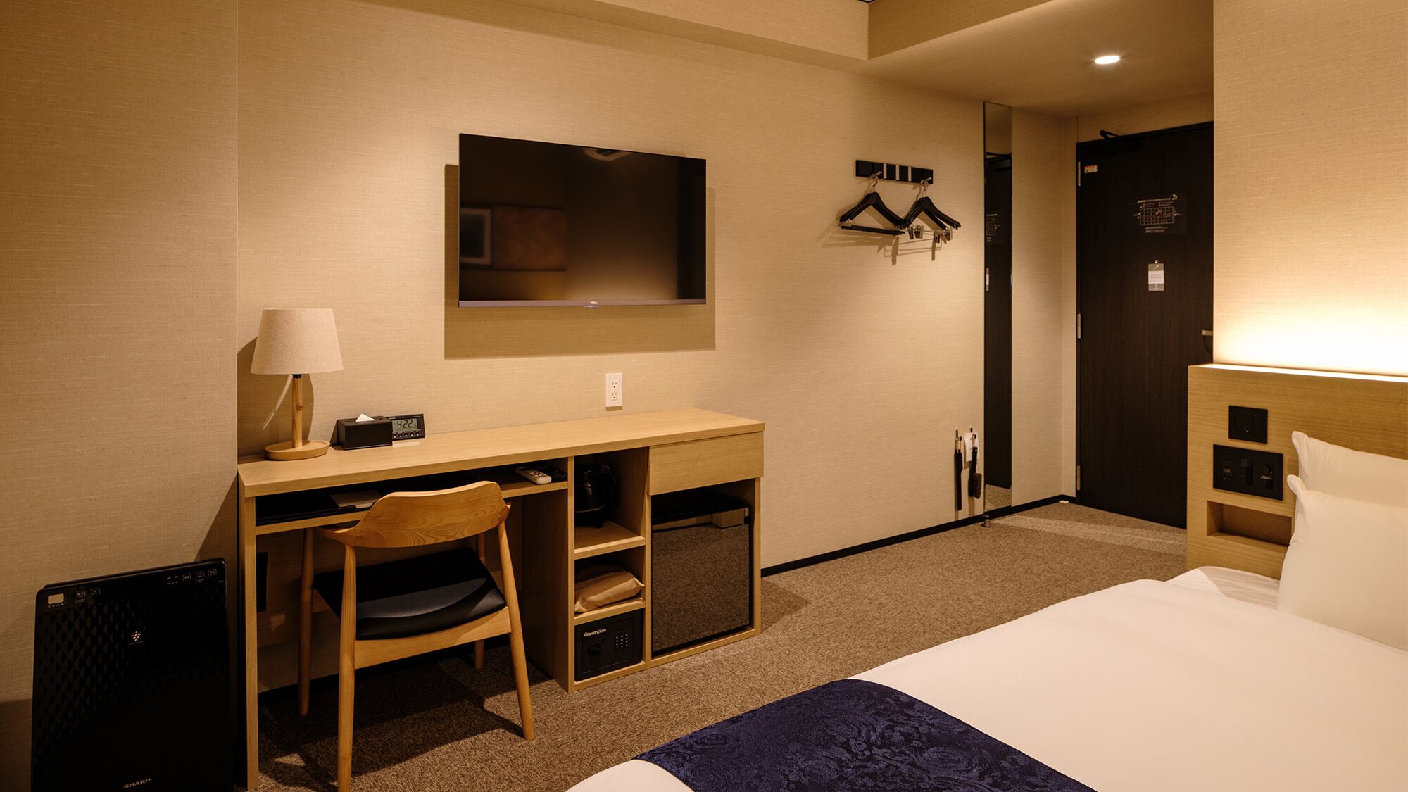 Ein Hotelzimmer mit Bett, Schreibtisch, Stuhl, Lampe, Uhr und Spiegel.