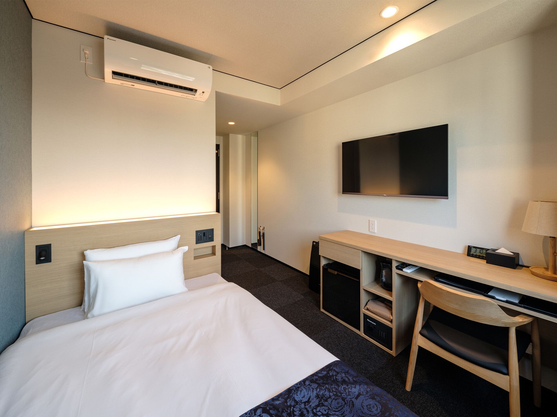 Quarto de hotel com cama, escrivaninha, cadeira, televisão e ar condicionado.