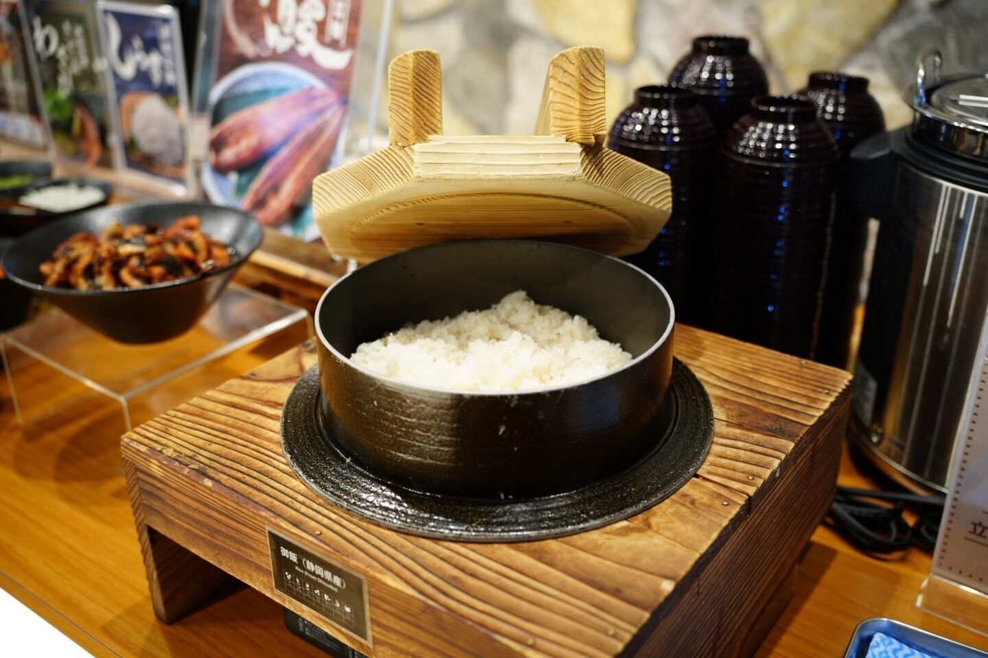 Una mesa de madera con un tazón de arroz, un cuenco de madera con palillos y un recipiente negro.