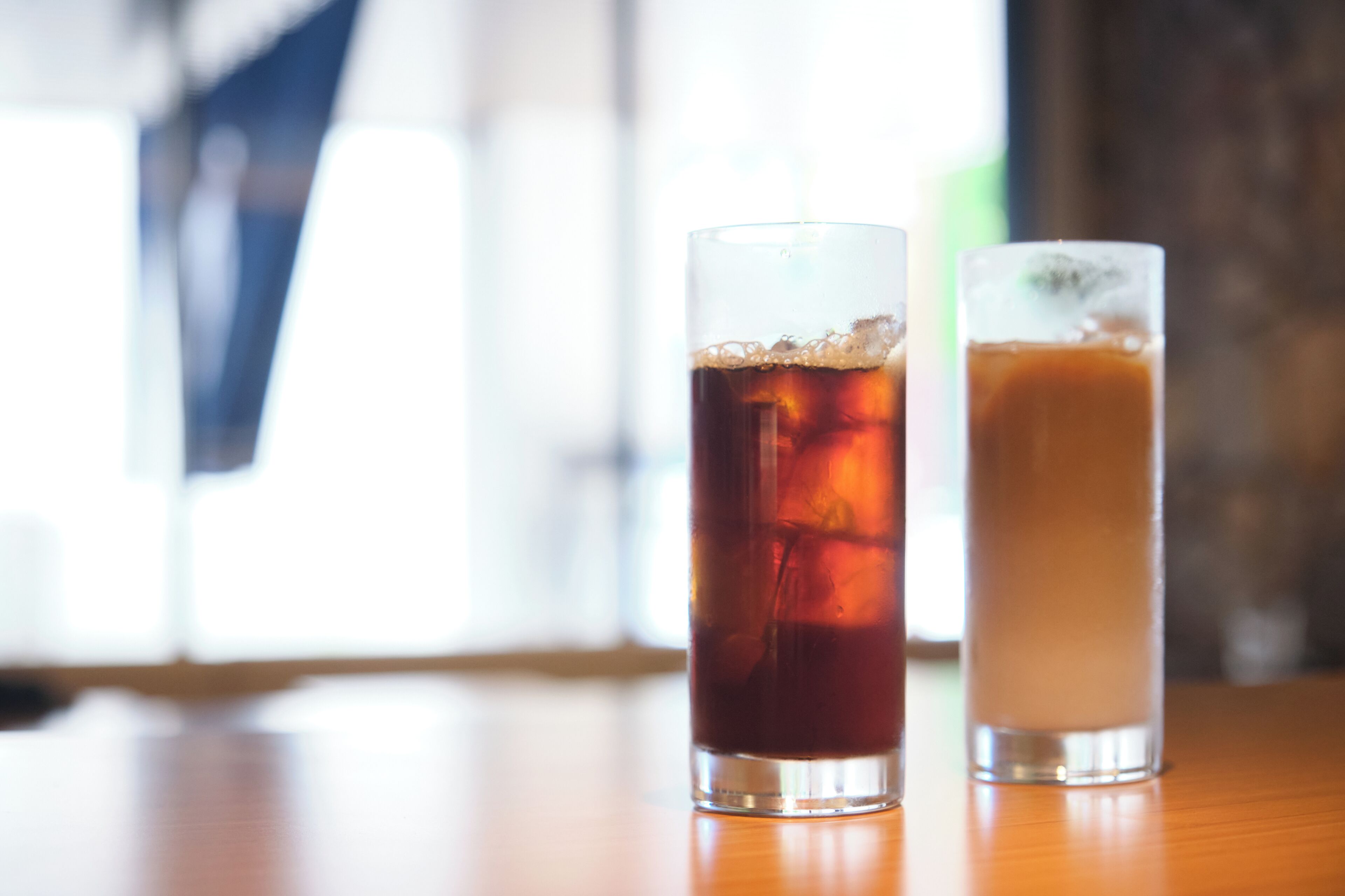 Dos vasos de bebidas heladas sobre una mesa de madera con un fondo desenfocado.