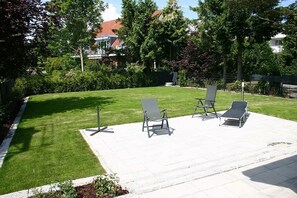 A patio area with four lounge chairs and a small table, surrounded by a well-maintained lawn and trees. - Villa Mare Apartment 4 - Villa Mare (Timmendorfer Strand)