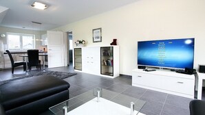 A modern living room with a flat-screen TV, a sofa, a coffee table, and a bookshelf.