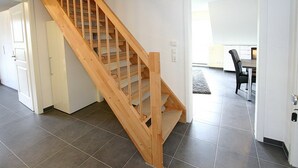 A wooden staircase in a modern interior with grey tiled flooring and white walls.