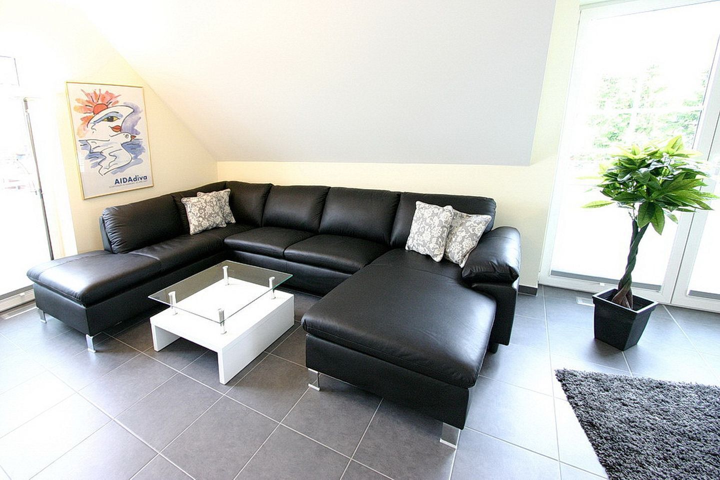 A modern living room with a black leather sectional sofa, a glass coffee table, and a potted plant.