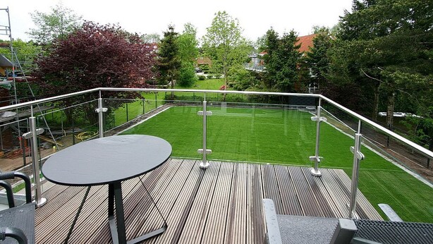 A wooden deck with a metal railing, a round table, and a chair.