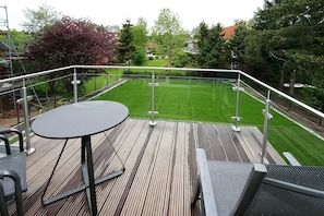 Eine Holzterrasse mit Metallgeländer, einem runden Tisch und einem Stuhl.