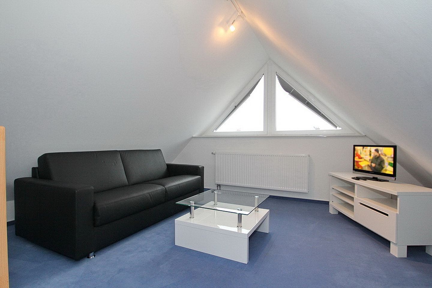 En moderne loftlejlighed med en sort lædersofa, et glas sofabord, et hvidt TV-møbel og et stort vindue med naturligt lys.