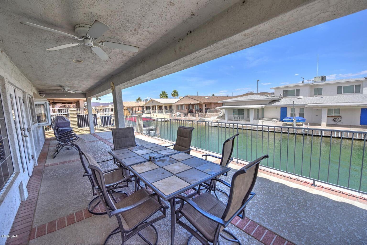 A covered outdoor area with a table and chairs, a ceiling fan, and a view of a marina with boats.