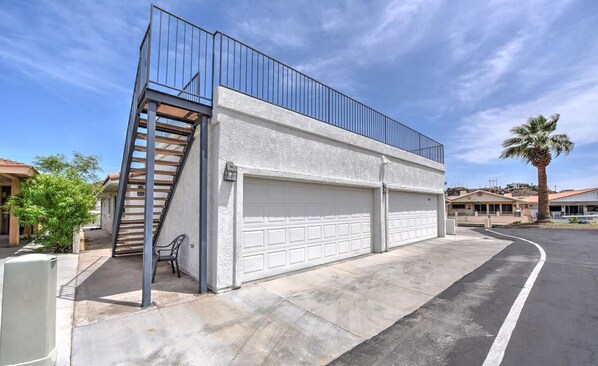 Un garaje residencial con fachada blanca, una escalera metálica y una puerta de garaje blanca.