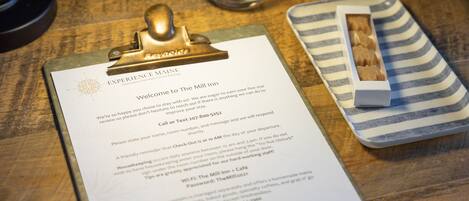 A welcome sign, a lamp, two glasses, a clipboard with a menu, and a striped napkin holder on a wooden table.