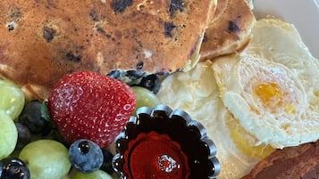 Ein Frühstücksteller mit Pfannkuchen, Eiern, Speck, Erdbeeren, Blaubeeren und Trauben.