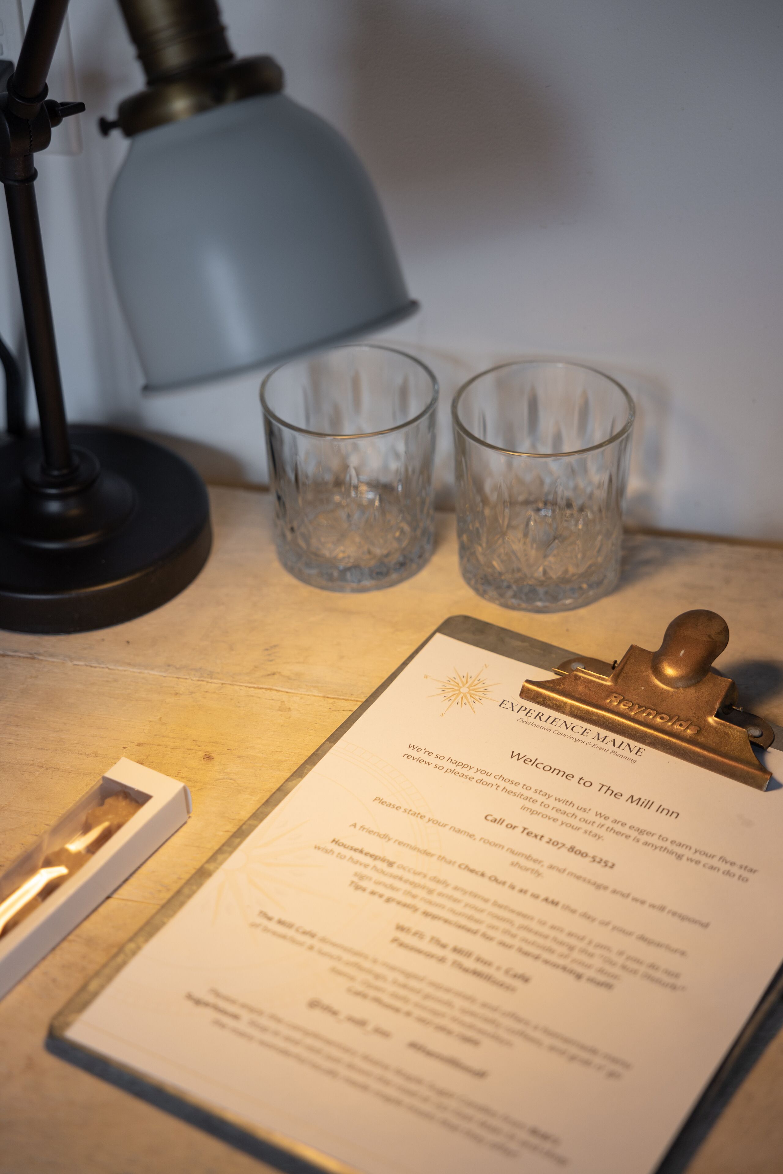 A clipboard with a welcome message for 'Experience Maine The Mill Inn' and two empty glasses on a table.