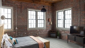 Una habitación con cama, televisión, planta y ventanas amplias.