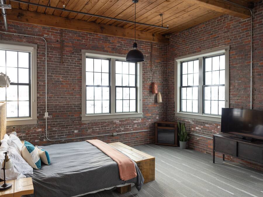 A room with a bed, a television, a plant, and large windows.