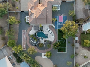 An aerial view of a residential property with a swimming pool, tennis courts, and a landscaped garden.