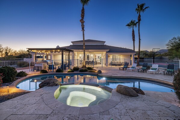 A pool with a hot tub, palm trees, and outdoor seating.