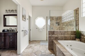 A bathroom with a large bathtub, a shower area, a vanity with a mirror, and a window.
