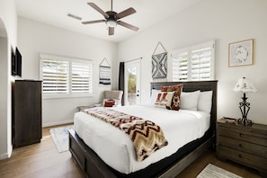 A bedroom with a bed, a bedside table, a lamp, a chair, and a ceiling fan.