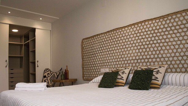 Un letto rifatto con lenzuola a righe, una testiera con motivo geometrico e un comodino con delle bottiglie.