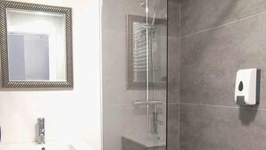 Un bagno moderno con doccia vetrata, un mobile lavabo con specchio e un dispenser per sapone.