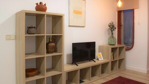 Een woonkamer met houten wandplanken, een flatscreen televisie, een vaas met bloemen en een rood vloerkleed.