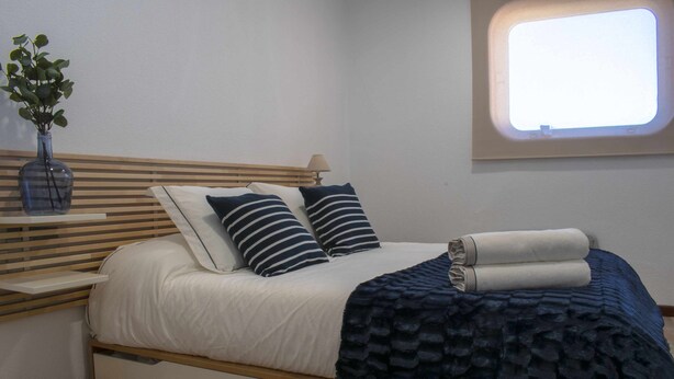Een slaapkamer met een bed, kussens, een nachtkastje, een lamp, een raam en een plant.