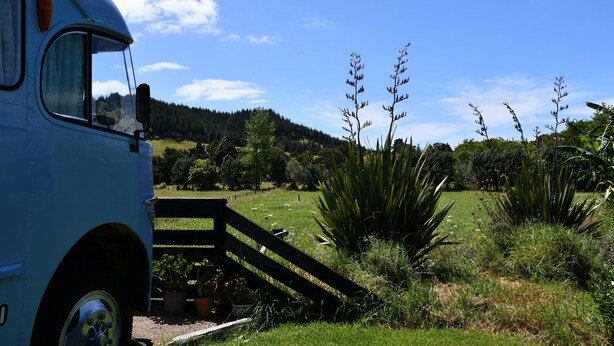 A blue bus parked in a grassy area with a wooden deck leading to a building. - Evi the school bus at Oromahoe Downs Farm (Kerikeri)
