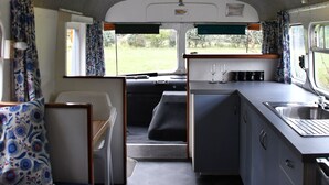 A compact kitchen area with a sink, countertop, and window. There is a small seating area with a bench and a chair. - Evi the school bus at Oromahoe Downs Farm (Kerikeri)