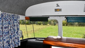A camper van interior with a view of a grassy field through the windows. - Evi the school bus at Oromahoe Downs Farm (Kerikeri)