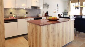 Une cuisine moderne avec des meubles blancs, un îlot central en bois et des luminaires suspendus.