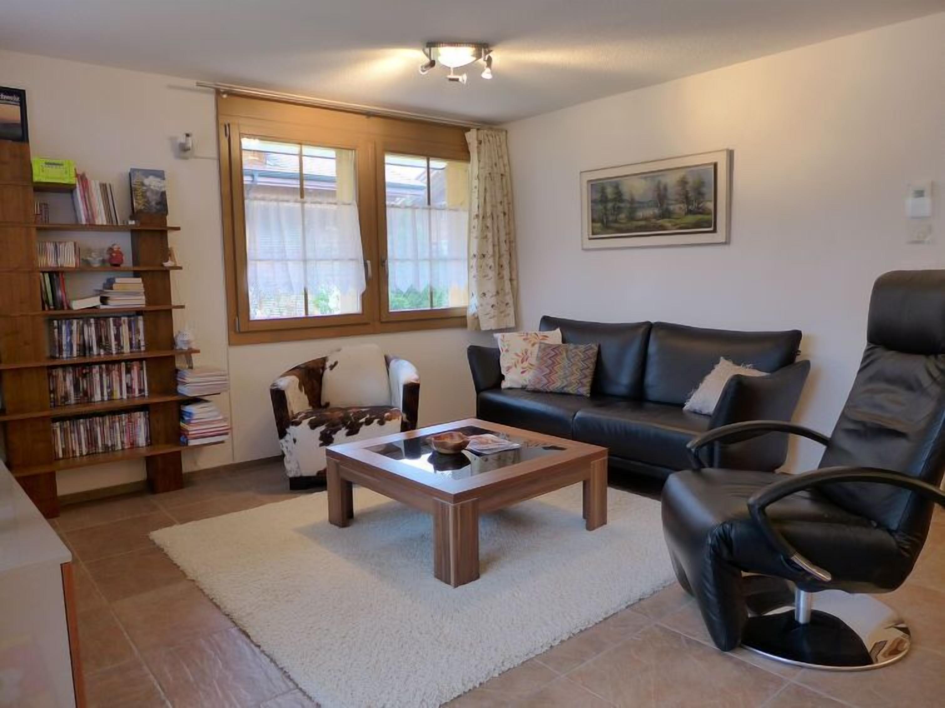 A living room with a sofa, a coffee table, a bookshelf, and a window with curtains.