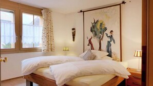 Un lit double avec une literie blanche, une tête de lit en bois et un tableau représentant un arbre et des personnages accroché au mur.