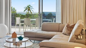 A modern living room with a beige sofa, a round coffee table, and a view of the ocean through large windows.