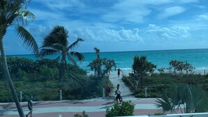 Un balcón con vistas a la playa, palmeras y un cielo despejado.